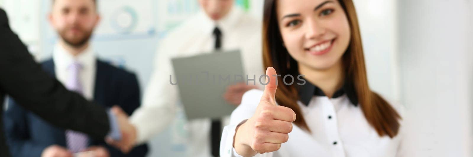 Businesswoman feels confident in team and thumbs up gesture. Happy businesswoman showing thumbs up and smiling colleagues standing in background