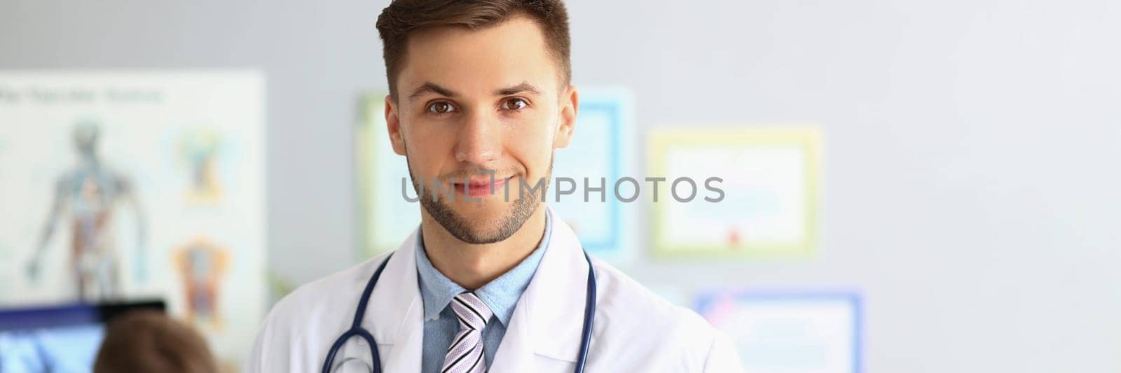 Friendly male general practitioner standing in office by kuprevich