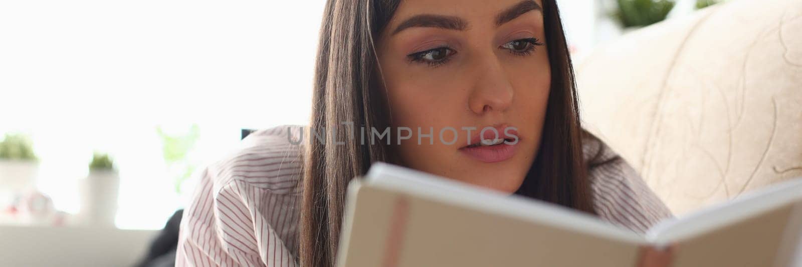 Portrait of pensive smart woman reading book at home and relaxing on sofa. Home leisure concept