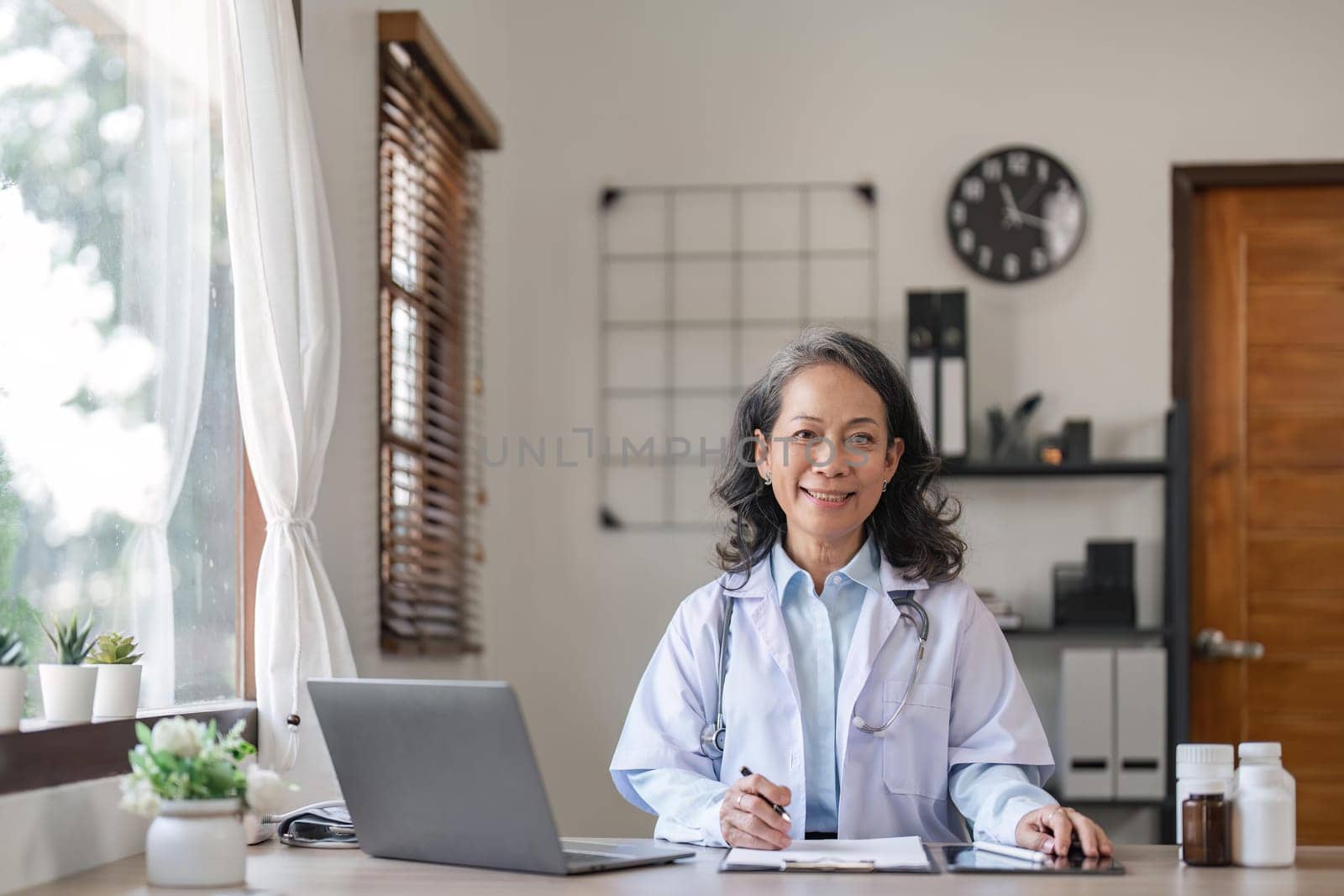 Portrait of smiling young Senior female doctor smiling sit at desk in hospital or private clinic, of happy positive female doctor in white medical uniform at workplace, healthcare.