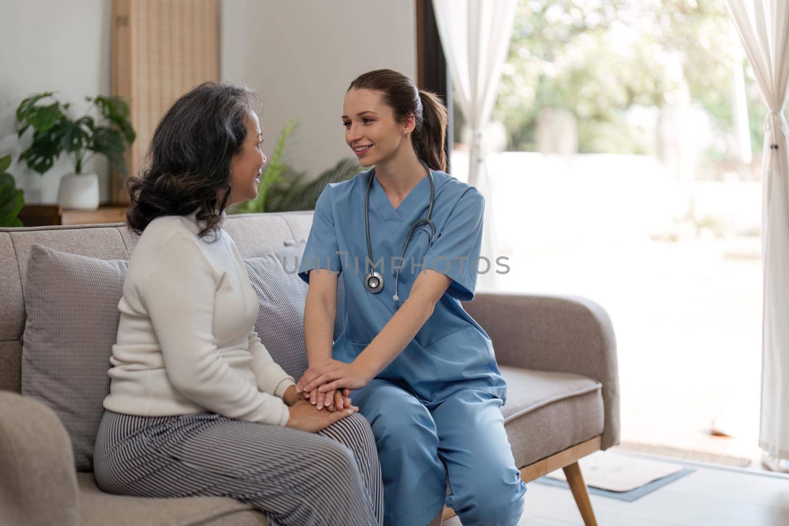 caregiver with senior woman and holding hands for care indoors. Retirement, consulting and professional female nurse with elderly person smiling together for healthcare support at nursing home.