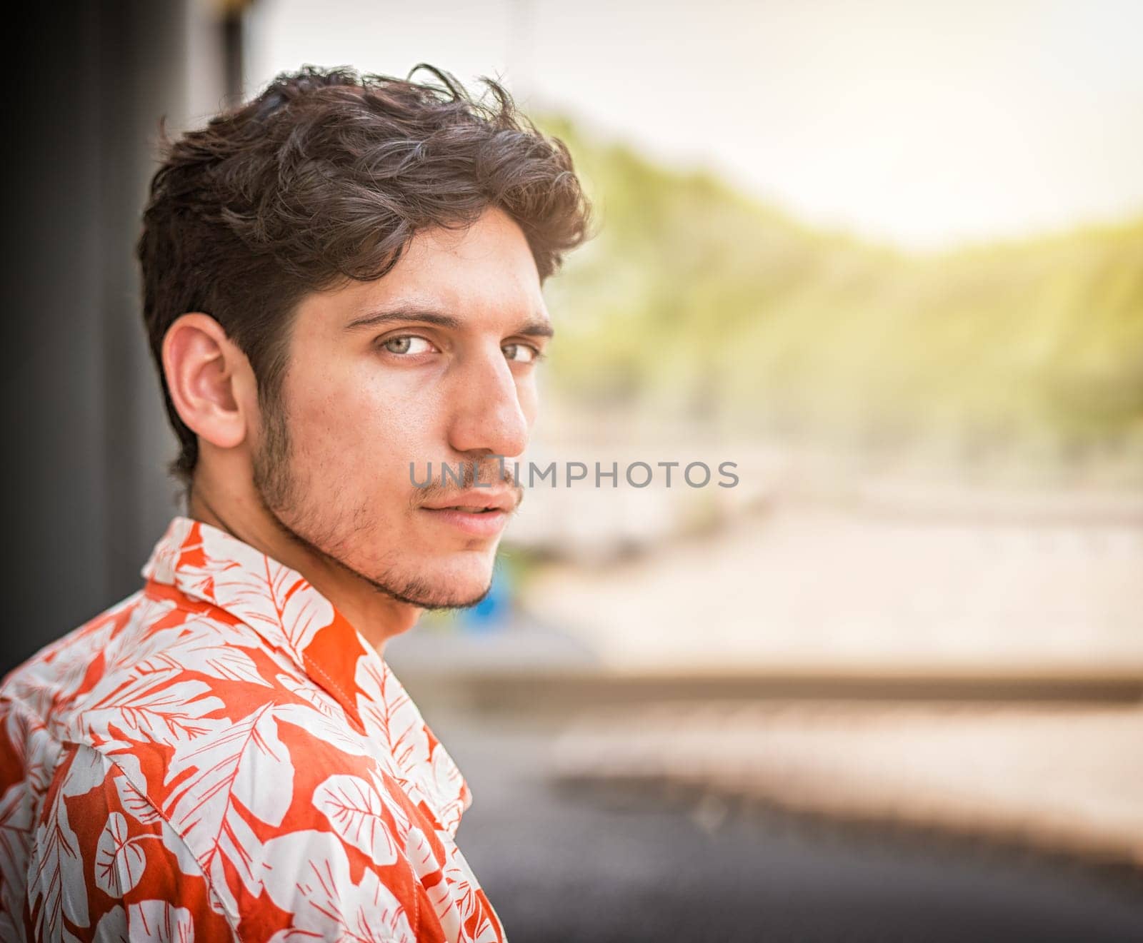 Headshot of one handsome young man with green eyes in urban setting, looking at camera, wearing shirt