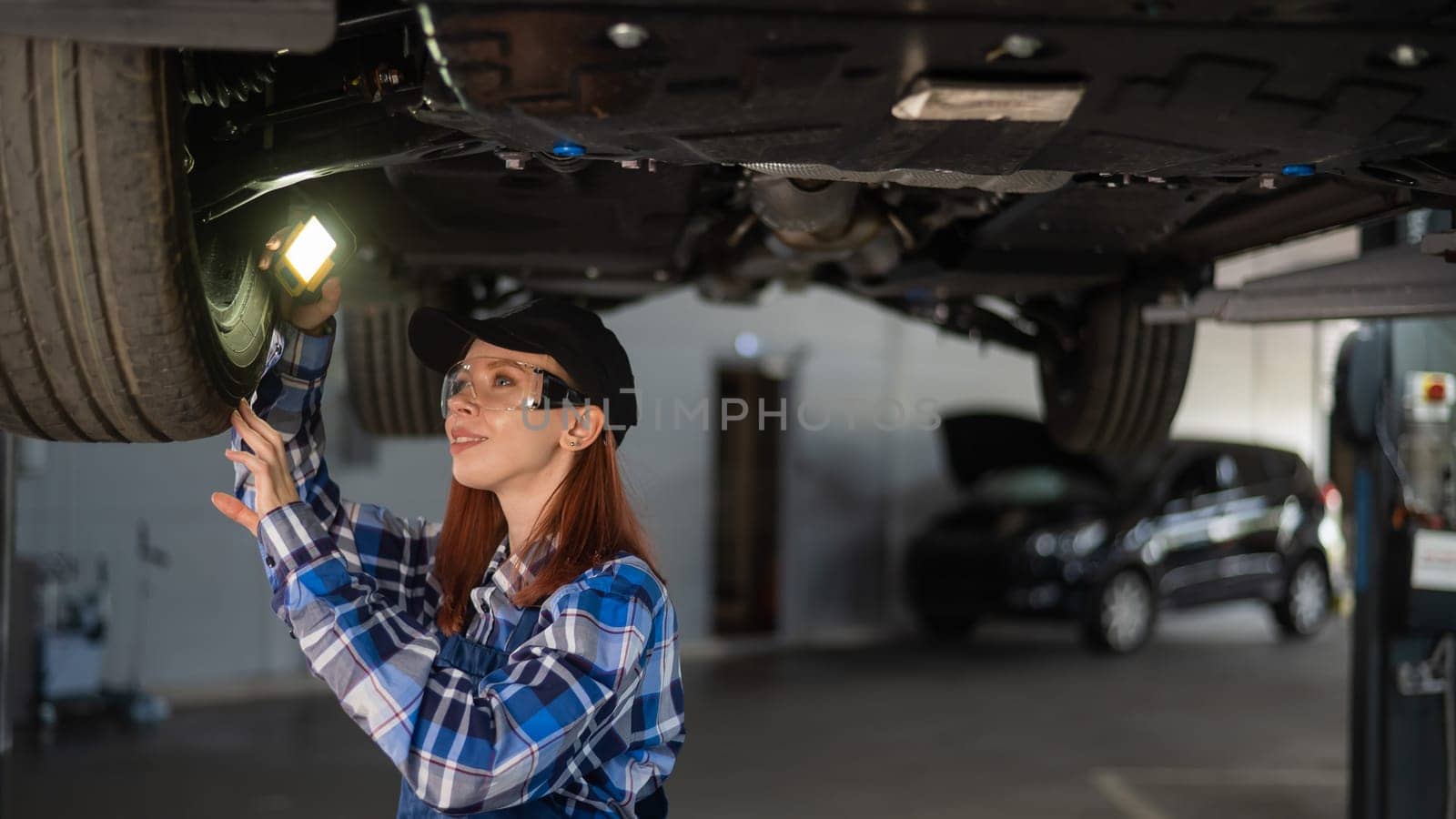 A female mechanic inspects a lifted car. A girl at a man's work. by mrwed54