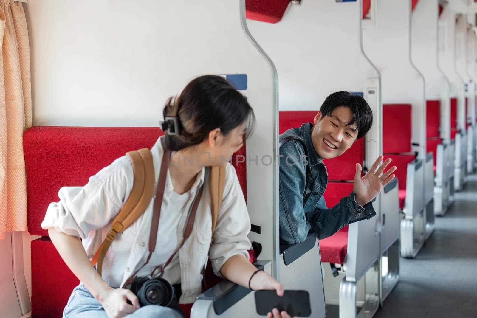 friendly and young Asian male traveler waves his hand, greeting a new friend during the trip on a train. Friendship and traveling concepts.