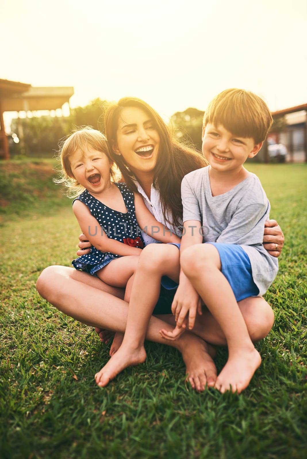 Mother, happy kids or hug playing on grass for fun bonding in summer outside a house in nature. Funny mom hugging playful children on garden playground outdoors with happiness of family together.