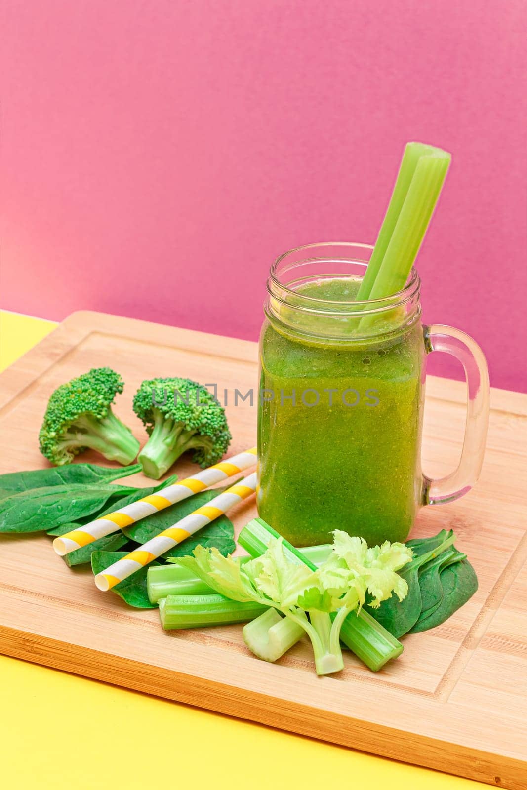 Fresh Green Smoothie of Apple, Celery, and Spinach in Glass Smoothie Jar with Yellow Cocktail Straw on Wooden Cutting Board. Vegan Detox Drink. Vegetarian Culture. Healthy Eating and Fruit Diet