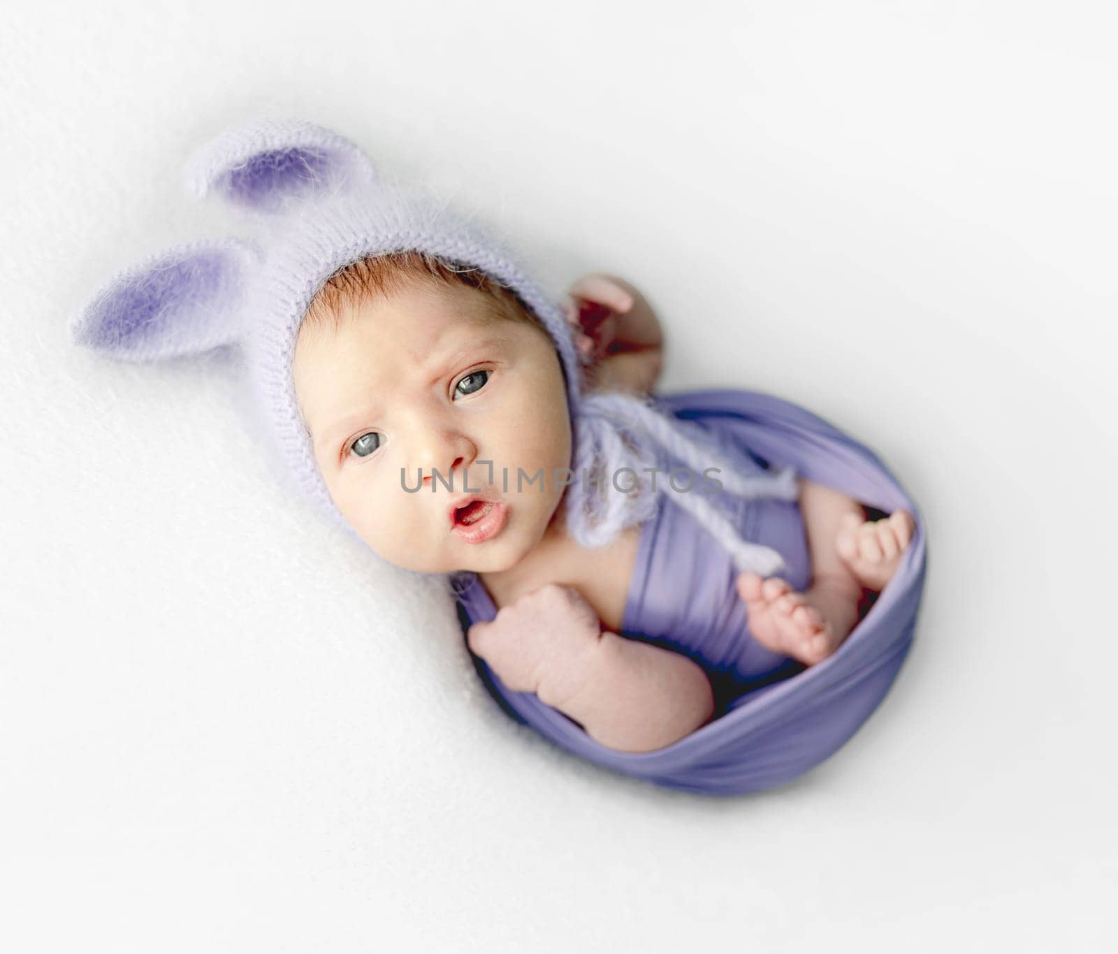 Newborn baby girl with beautiful blue eyes wearing knitted hat with banny ears studio portrait.