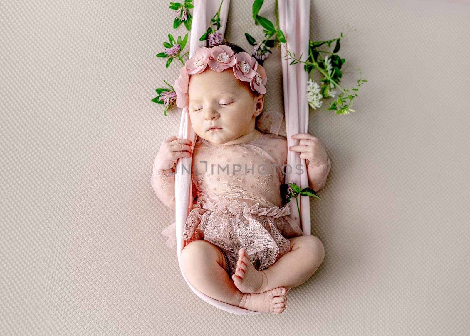 Newborn baby girl wearing dress and wreath sleeping in swing decorated with flowers. Cute infant child kid stylish studio portrait