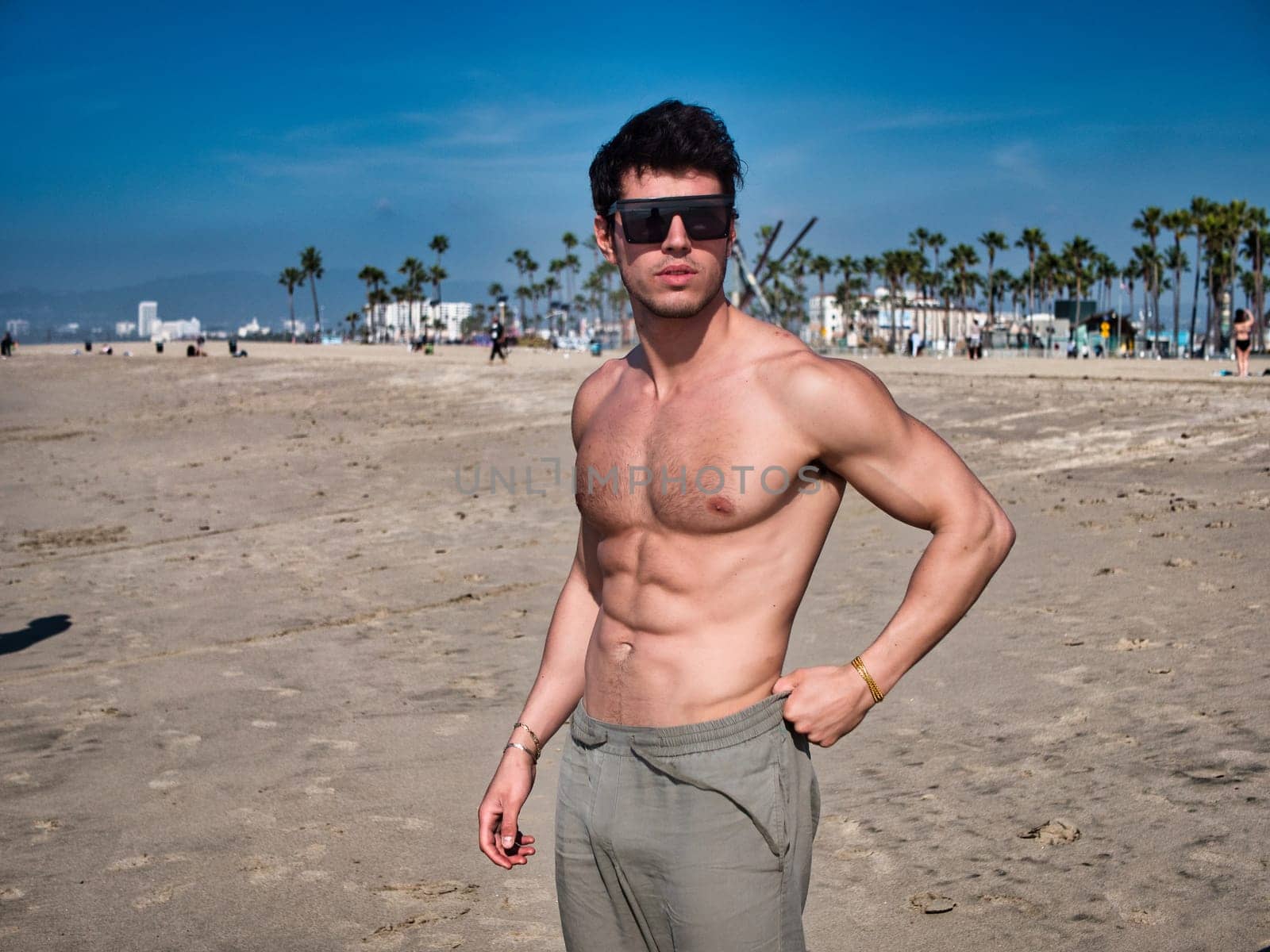 Handsome young man standing on a beach, shirtless wearing boxer shorts, showing muscular fit body in Venice Beach, California, USA