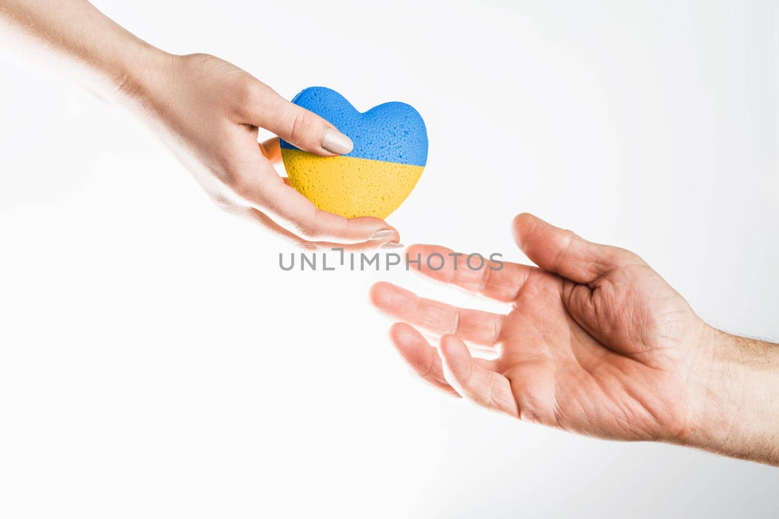 Female hand gives blue yellow ukraine heart to male hand on light background. concept needs help and support, truth will win
