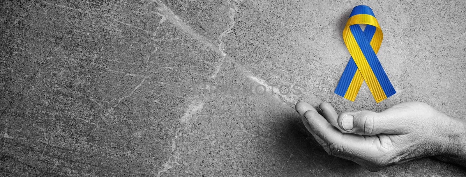 male hand with yellow and blue ribbon on marble background black and white color. concept needs help and support, truth will win