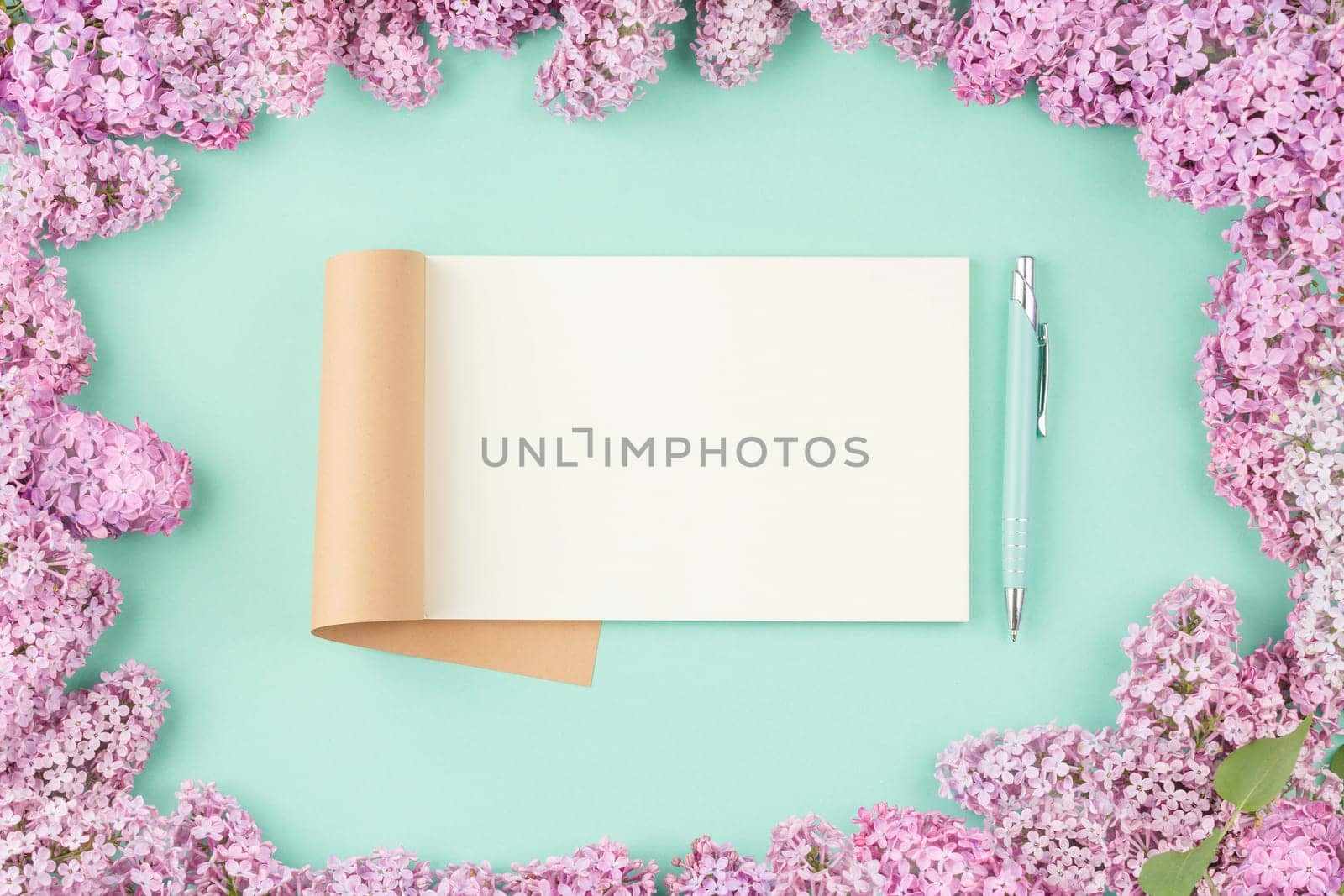 Open notebook with pen and lilac flowers on isolated cyan background. Open craft album. Top view.
