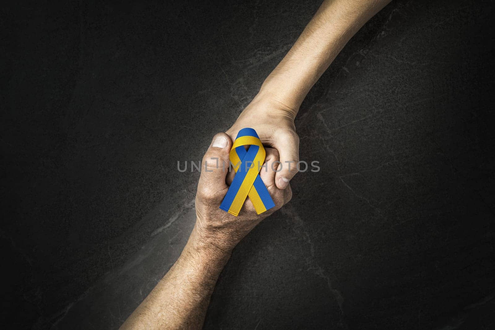 adult hand holding tight hand of child with yellow and blue ribbon on dark background. concept needs help and support, truth will win