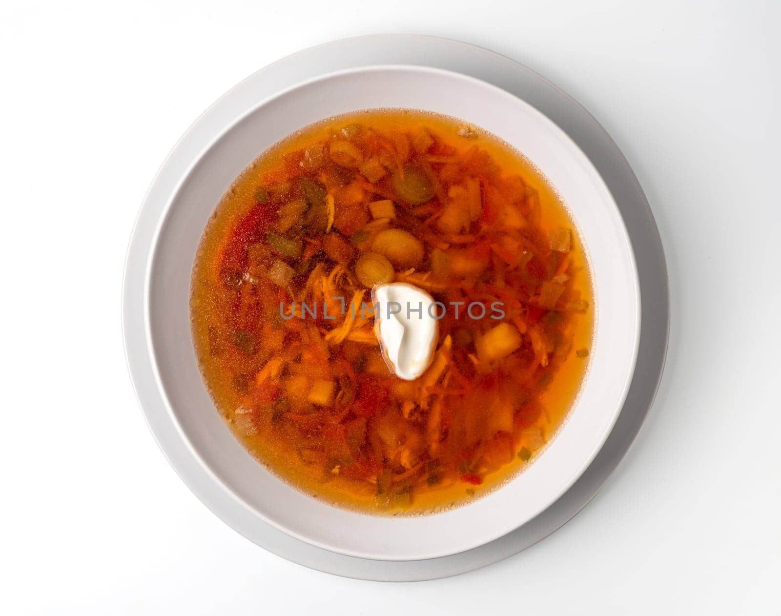 Bowl with chicken, beetroot and other vegetables soup. Perfect bright broth in italian minestrone style, isolated on white. Top view or flat lay.