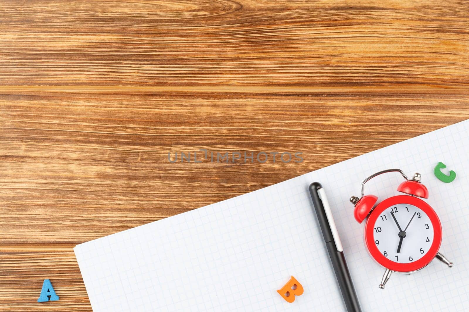 Open notebook with a pen on a wooden background. Study desk with red alarm clock and color letters abc. Flat lay. Back to school concept. Top view.