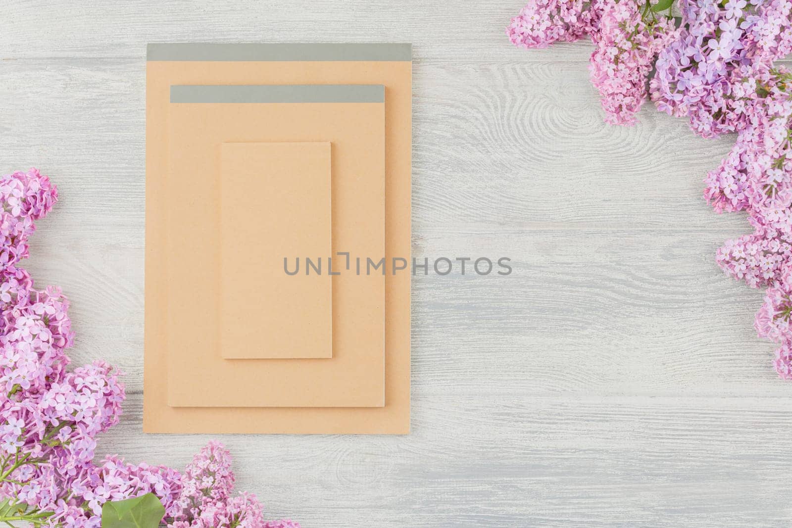 Notebook and lilac flowers on a white wooden background. Top view.