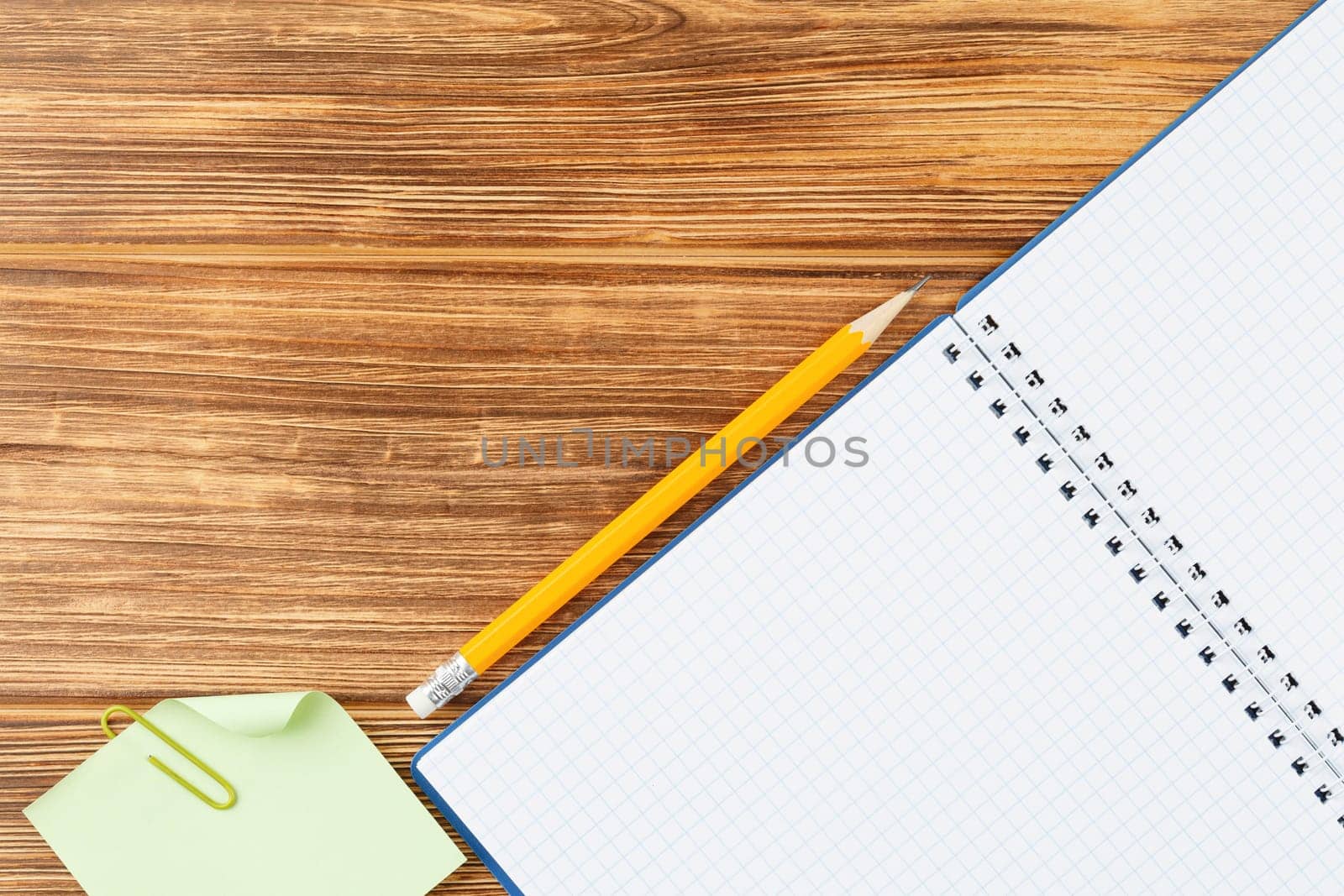 Open spiral notebook with pencil and note sheet on wooden background. Flat lay. Back to school concept. Study desk. Top view.