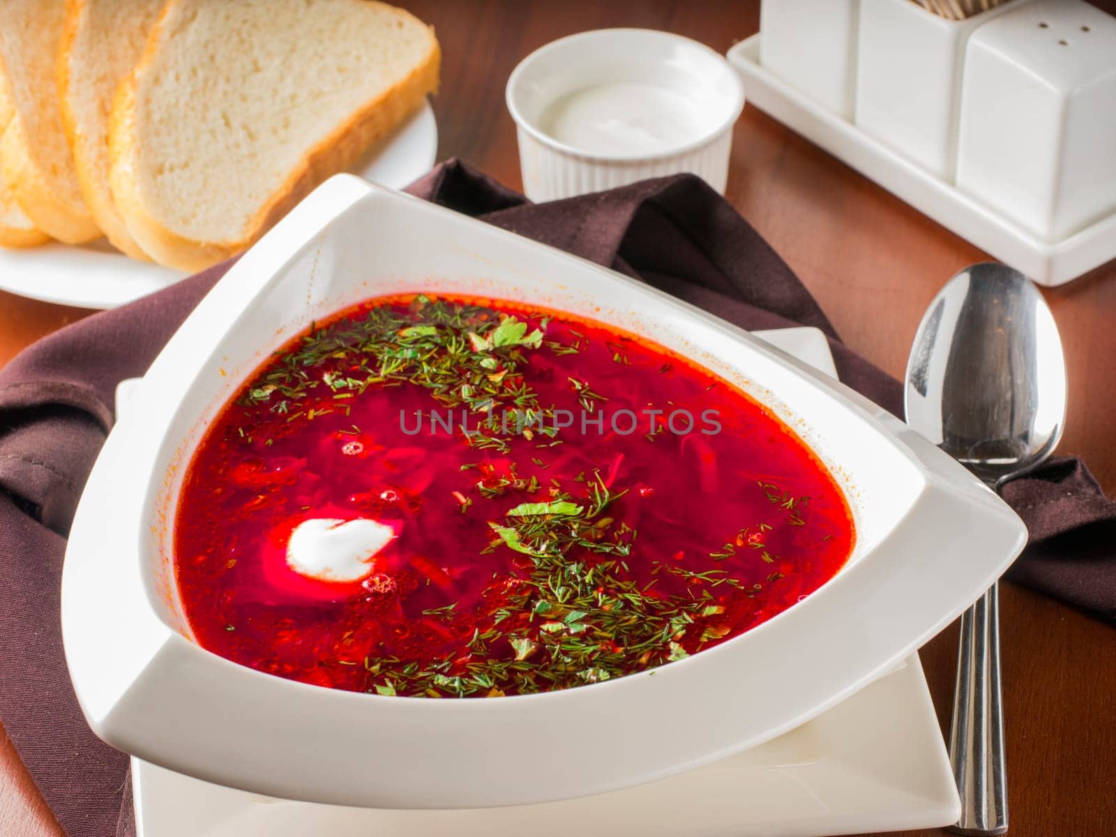 Ucrainian russian traditional beetroot soup - borsch in triangular white plate on dark brown wooden table in restaurant