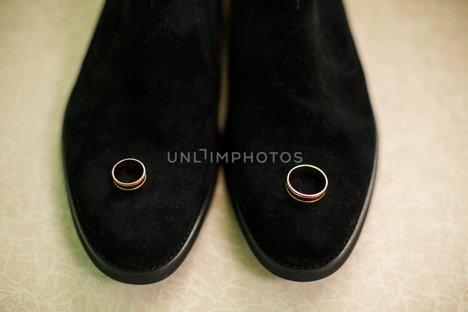 Gold wedding rings of the newlyweds lie next to men's shoes for the groom by Dmitrytph