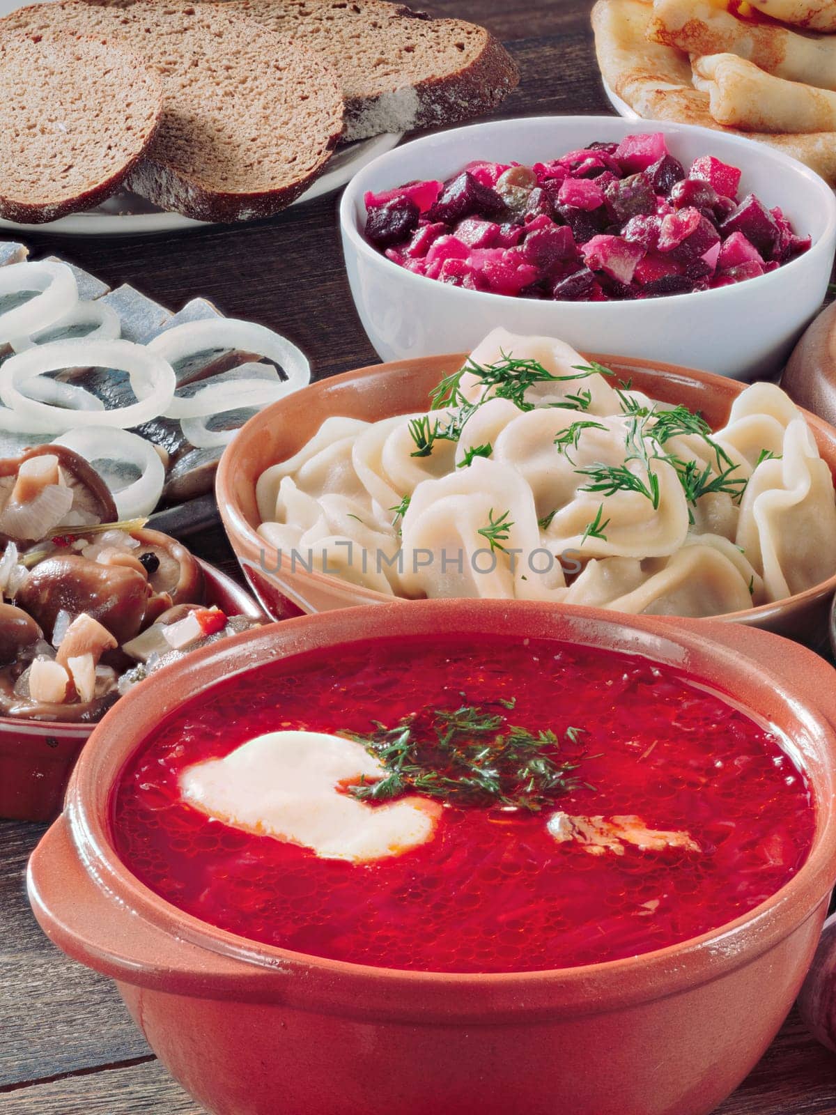 Perspective iew of wooden table with dishes of russian cuisine - borscht, pelmeni, herring, marinated mushrooms, vinaigrette, rye bread, pancakes. Vertical