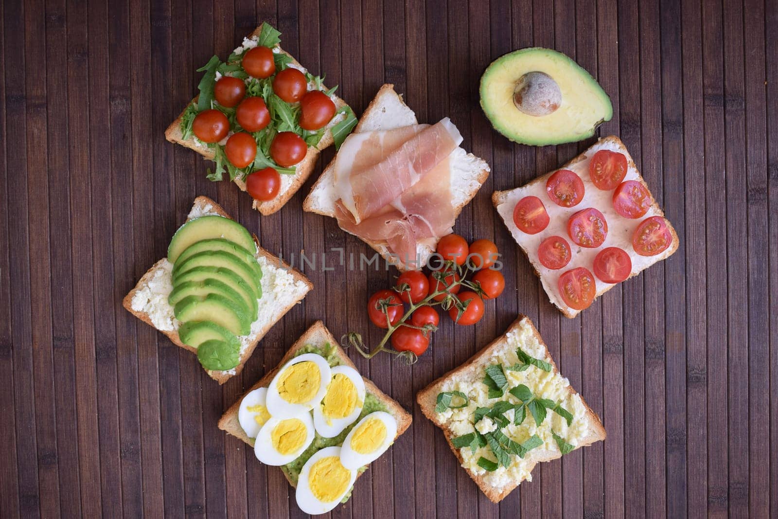 Healthy toast for breakfast with avocado, eggs, tomatoes, arugula etc.