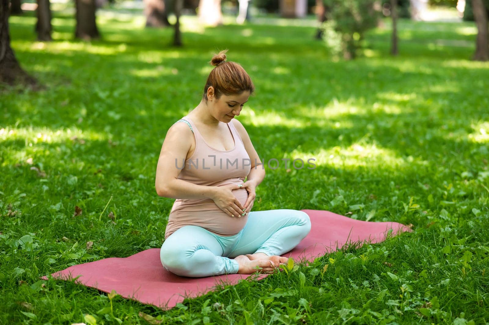 Prenatal yoga. Caucasian pregnant woman doing butterfly pose in the park