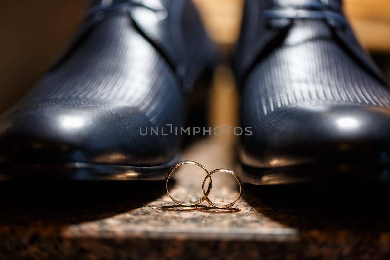 Gold wedding rings of the newlyweds lie next to men's shoes for the groom