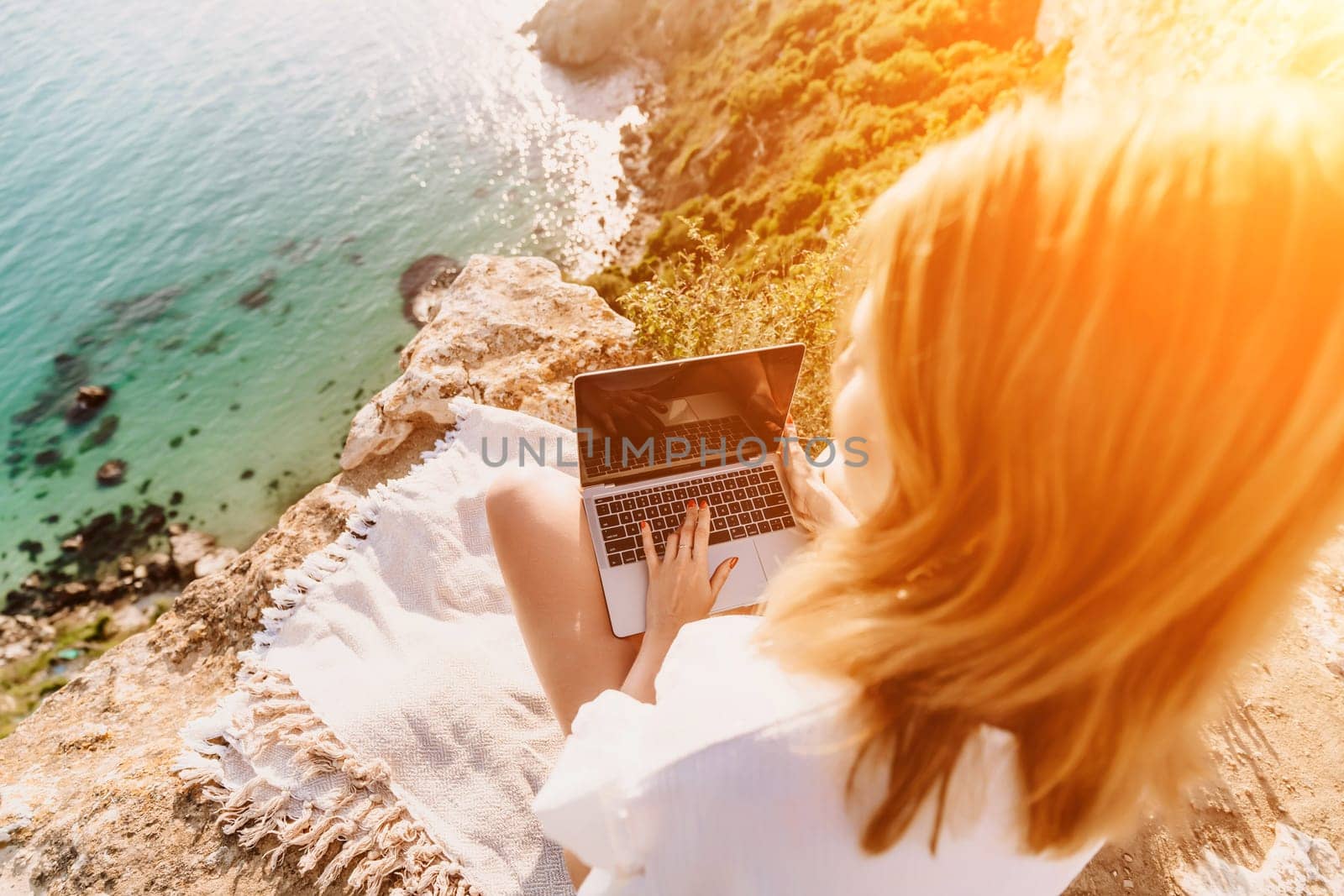 Freelance woman working on a laptop by the sea, typing away on the keyboard while enjoying the beautiful view, highlighting the idea of remote work. by Matiunina