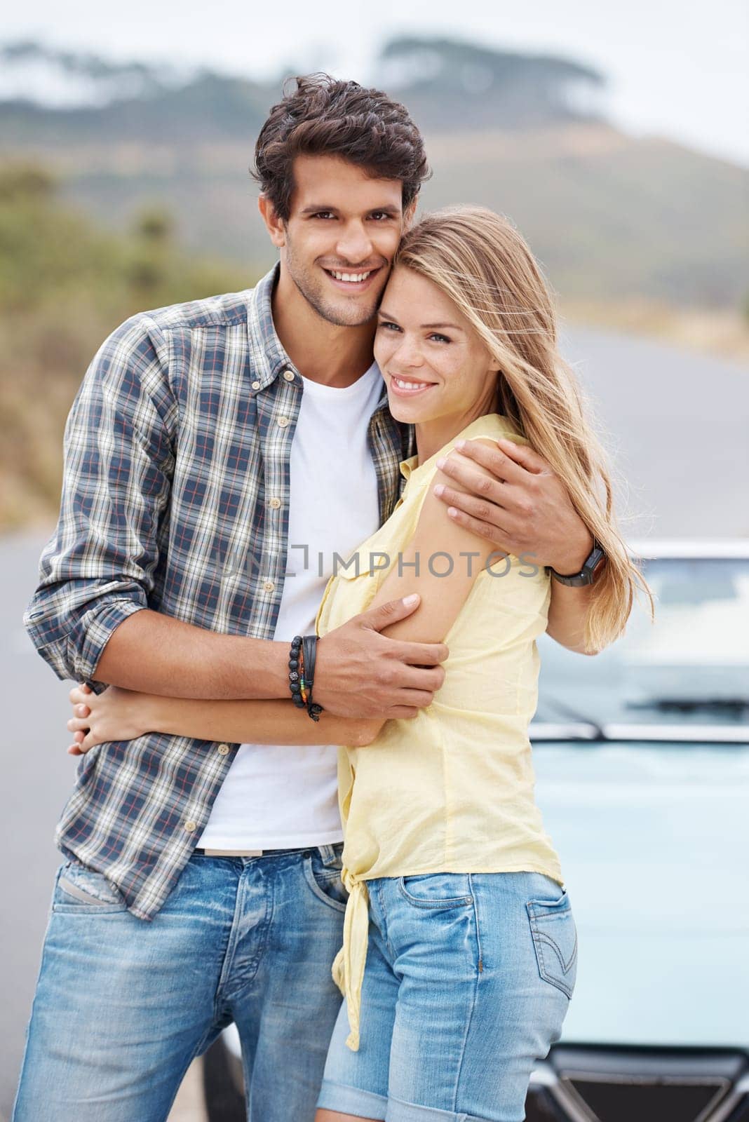 Theyre young and in love. A romantic young couple standing alongside their convertible while on a roadtrip. by YuriArcurs