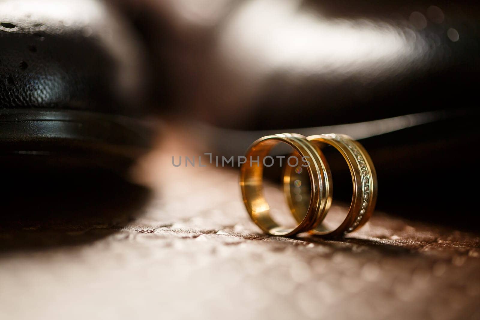 Gold wedding rings of the newlyweds lie next to men's shoes for the groom by Dmitrytph