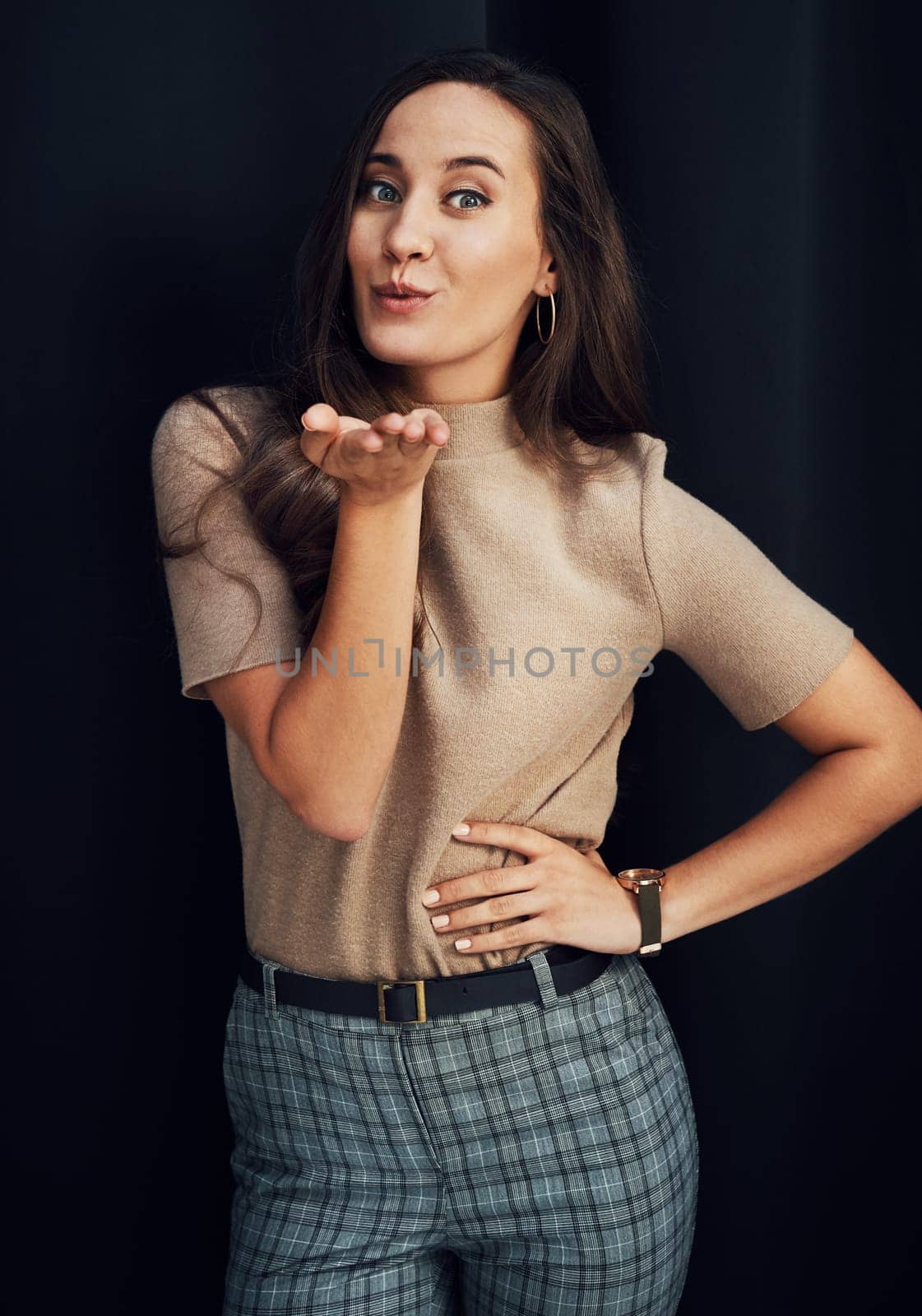 Fashion, beauty and woman blowing a kiss in studio on a dark background for love, romance or dating. Hand, portrait and smile with a happy young female standing indoors against a black wall alone.