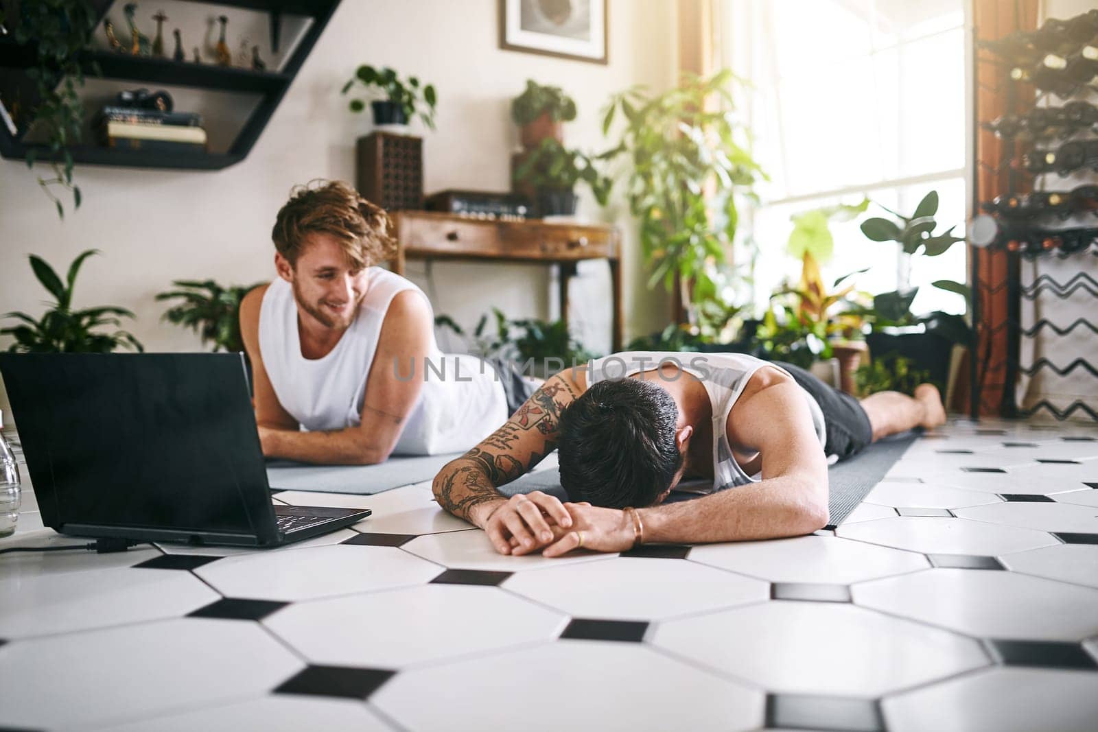 Aint no shame in a weak yoga game. two men taking a break after going through an online yoga routine at home. by YuriArcurs