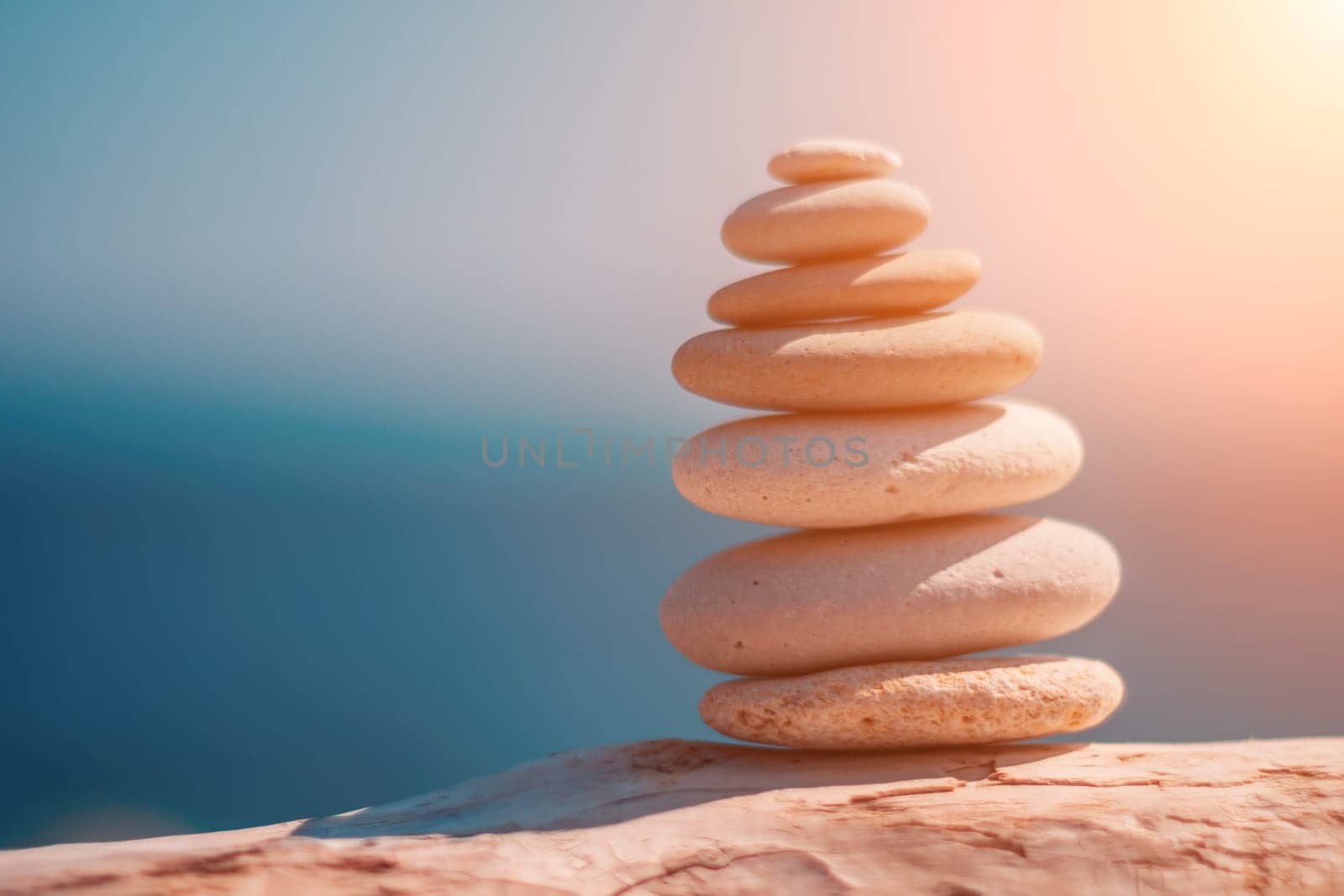 Balanced rock pyramid on sea pebbles beach, sunny day and clear sky at sunset. Golden sea bokeh on background. Selective focus, zen stones on sea beach, meditation, spa, harmony, calm, balance concept by panophotograph