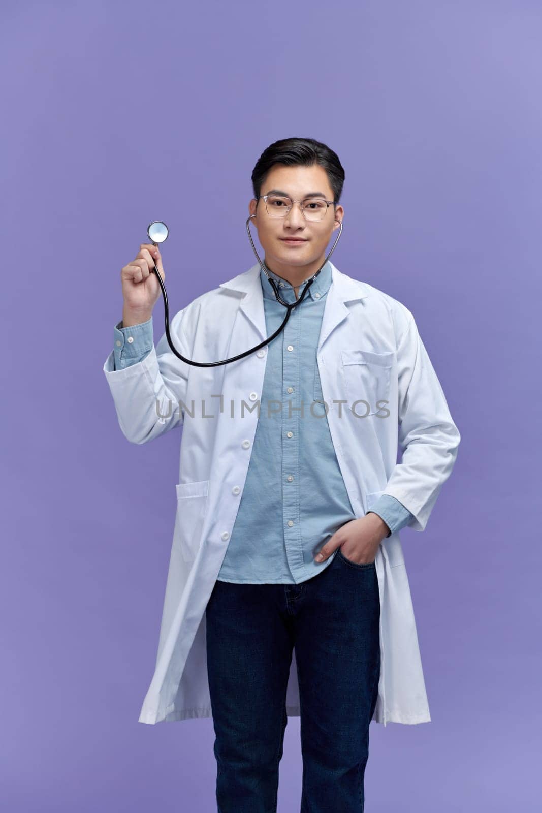 Handsome young medic holding a stethoscope, isolated over purple