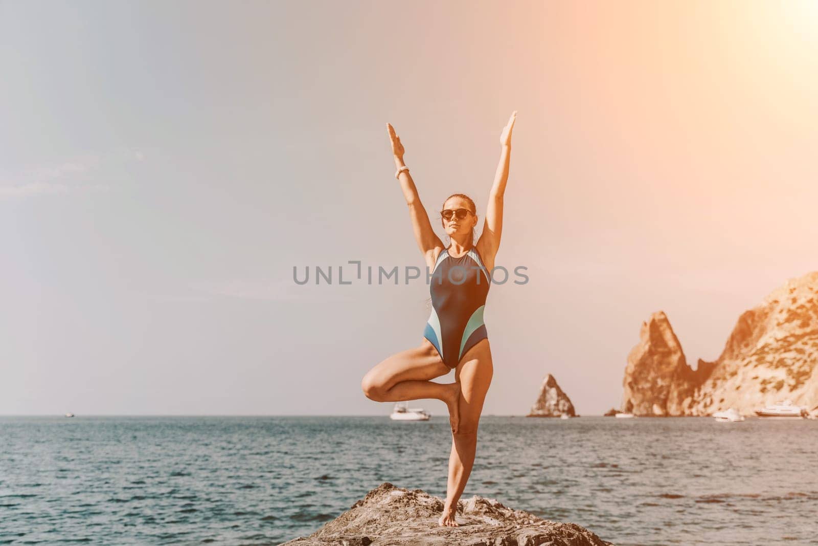 Yoga on the beach. A happy woman meditating in a yoga pose on the beach, surrounded by the ocean and rock mountains, promoting a healthy lifestyle outdoors in nature, and inspiring fitness concept