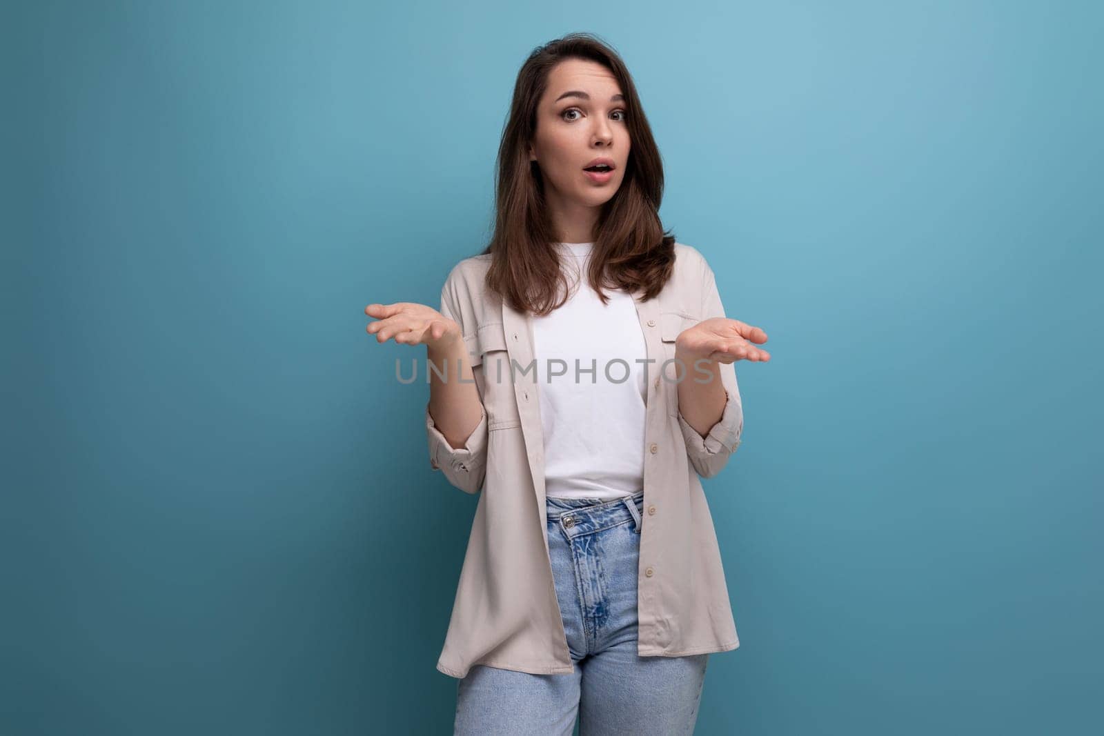 confused young dark-haired lady in informal clothes on a blue background.