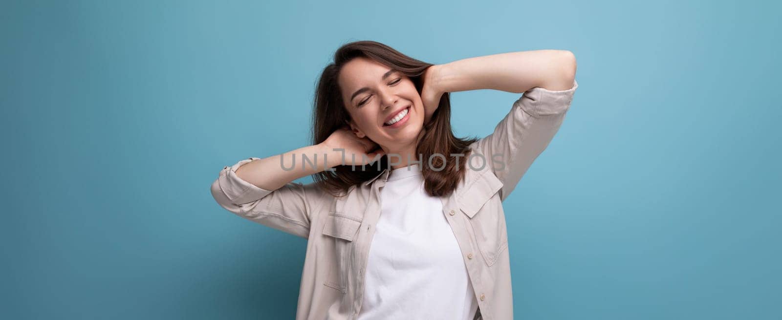 pretty 25 year old woman in a casual look smiles cutely on a blue background.