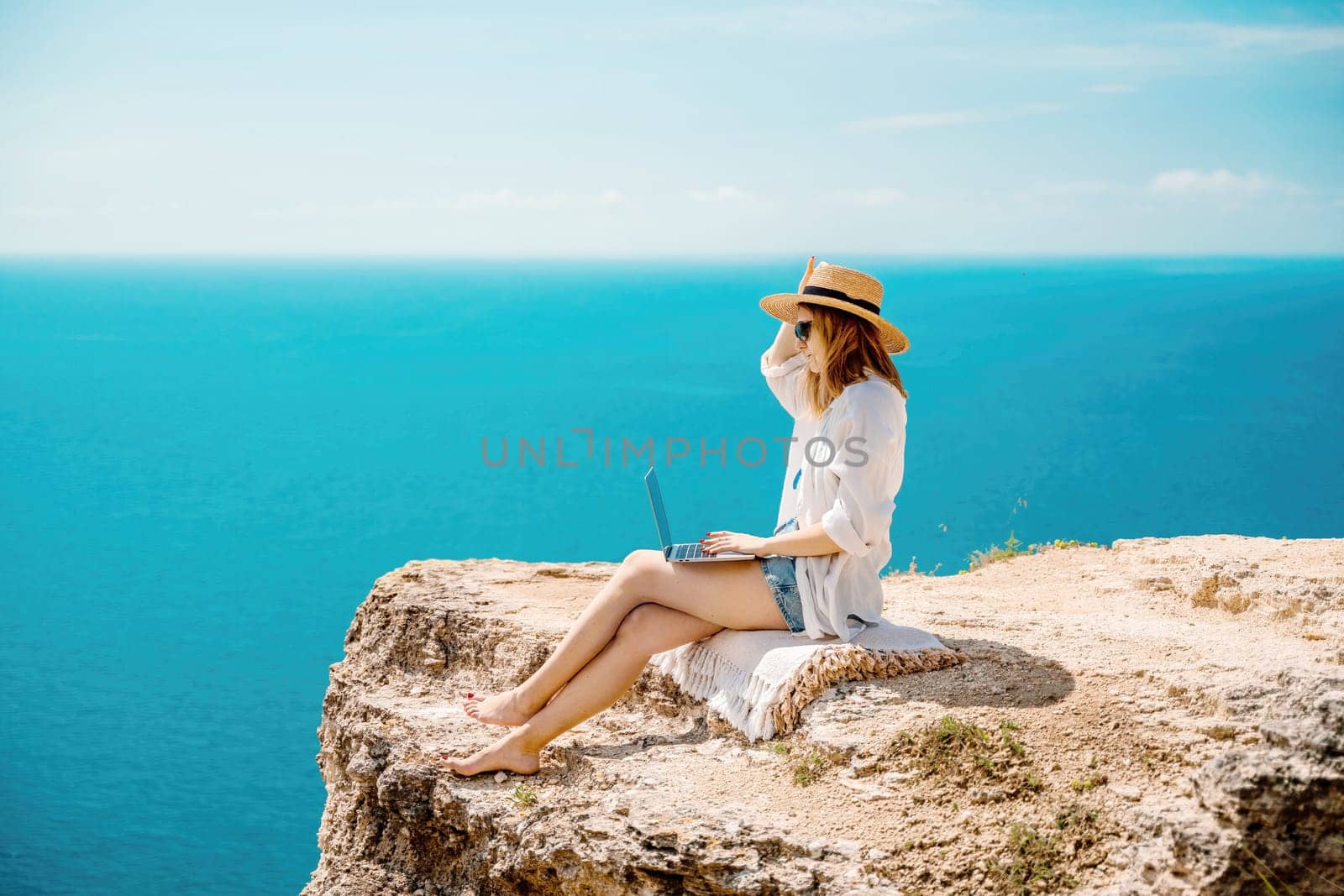 Freelance woman working on a laptop by the sea, typing away on the keyboard while enjoying the beautiful view, highlighting the idea of remote work