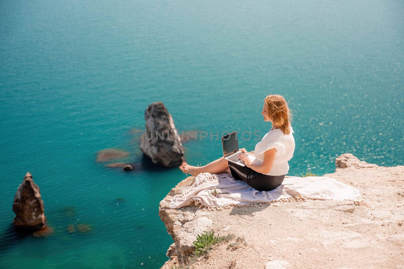 Freelance woman working on a laptop by the sea, typing away on the keyboard while enjoying the beautiful view, highlighting the idea of remote work. by Matiunina