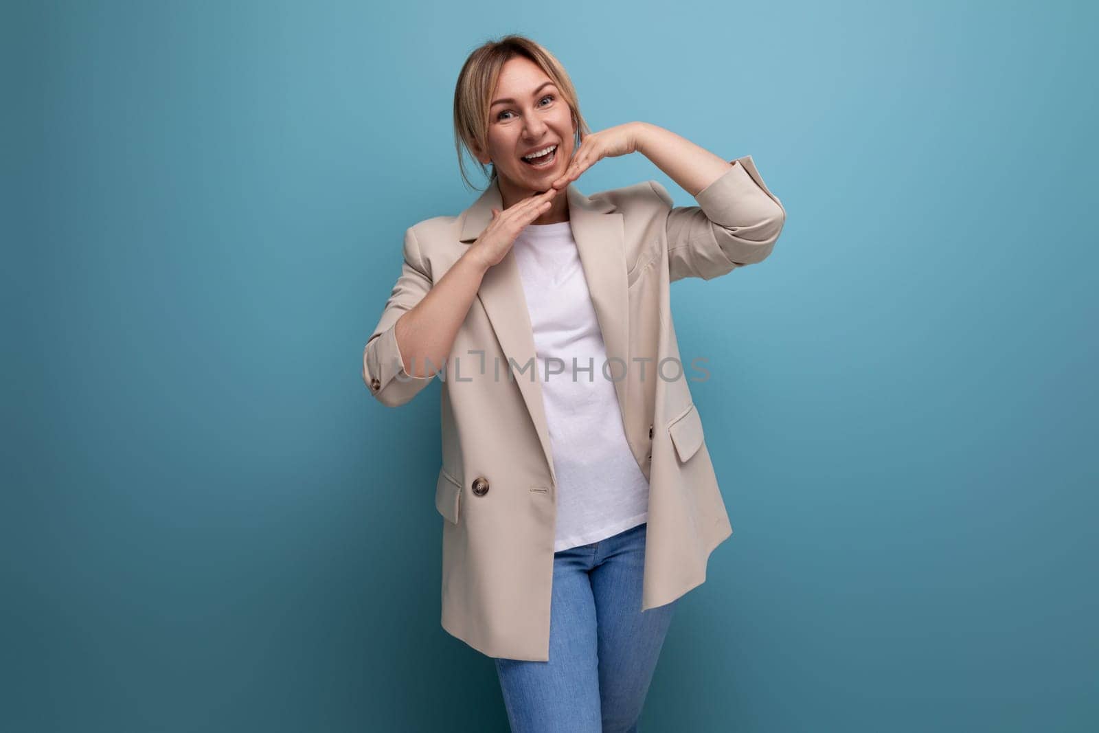 charming blonde young adult in jacket smiling on studio background.