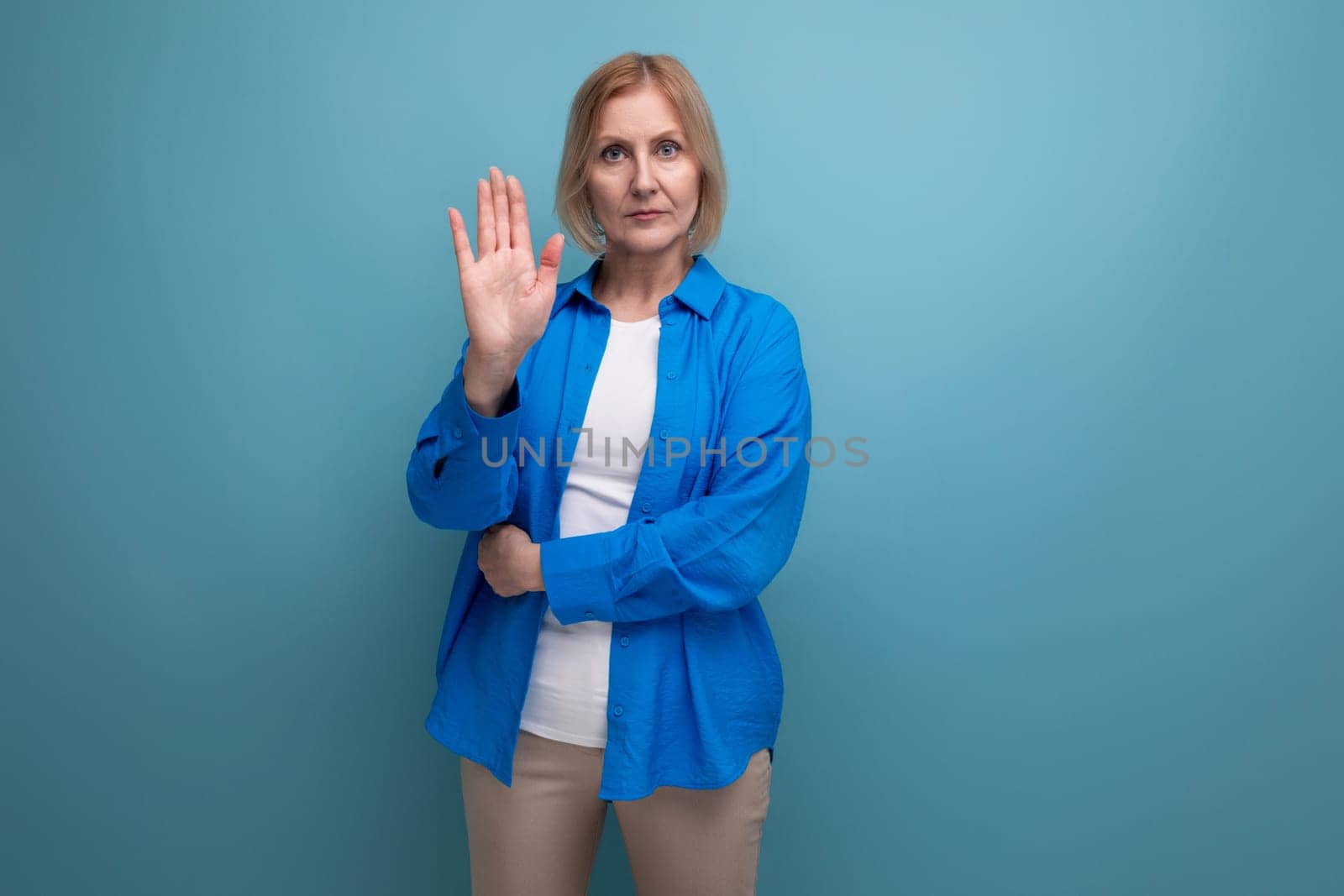 portrait of a blond attractive middle-aged woman in a casual stylish shirt on a blue background with copy space.