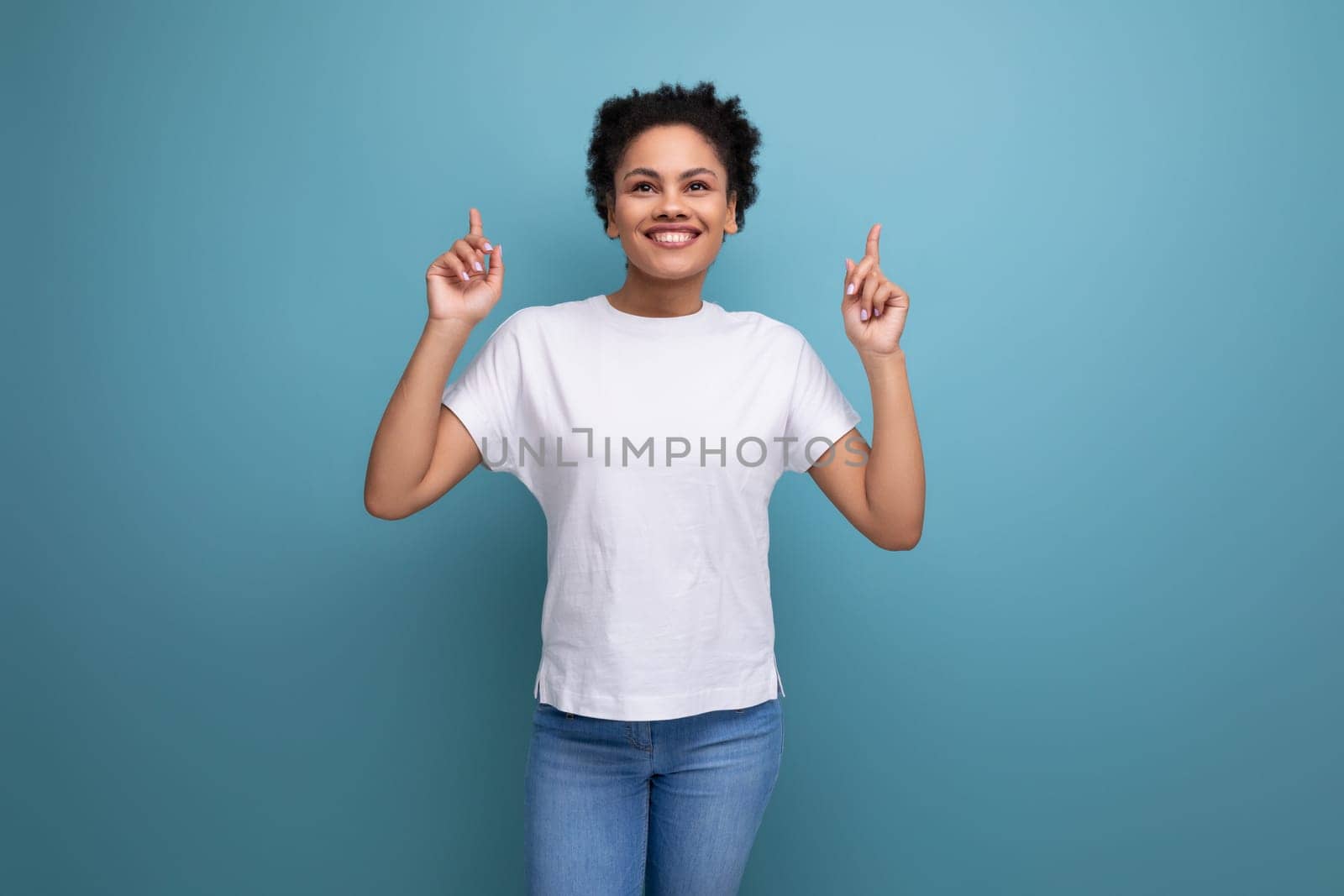 pretty young brunette hispanic woman in a white t-shirt shows with her hands on an empty space for advertising by TRMK