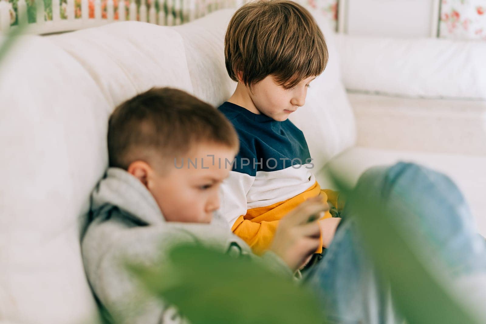 Cheerful two Childs boys playing online game, watching video on cellphone. Smiling kids using funny mobile apps, enjoying free leisure time at home on couch. Brothers play together at phone by Ostanina