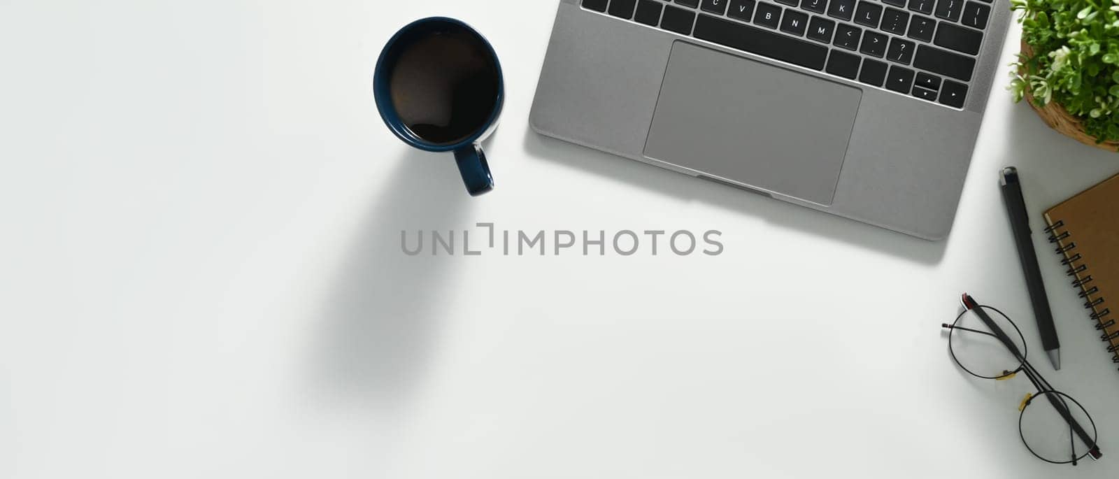 A cup of coffee, laptop, glasses and notebook on white office desk. Top view with coy space.