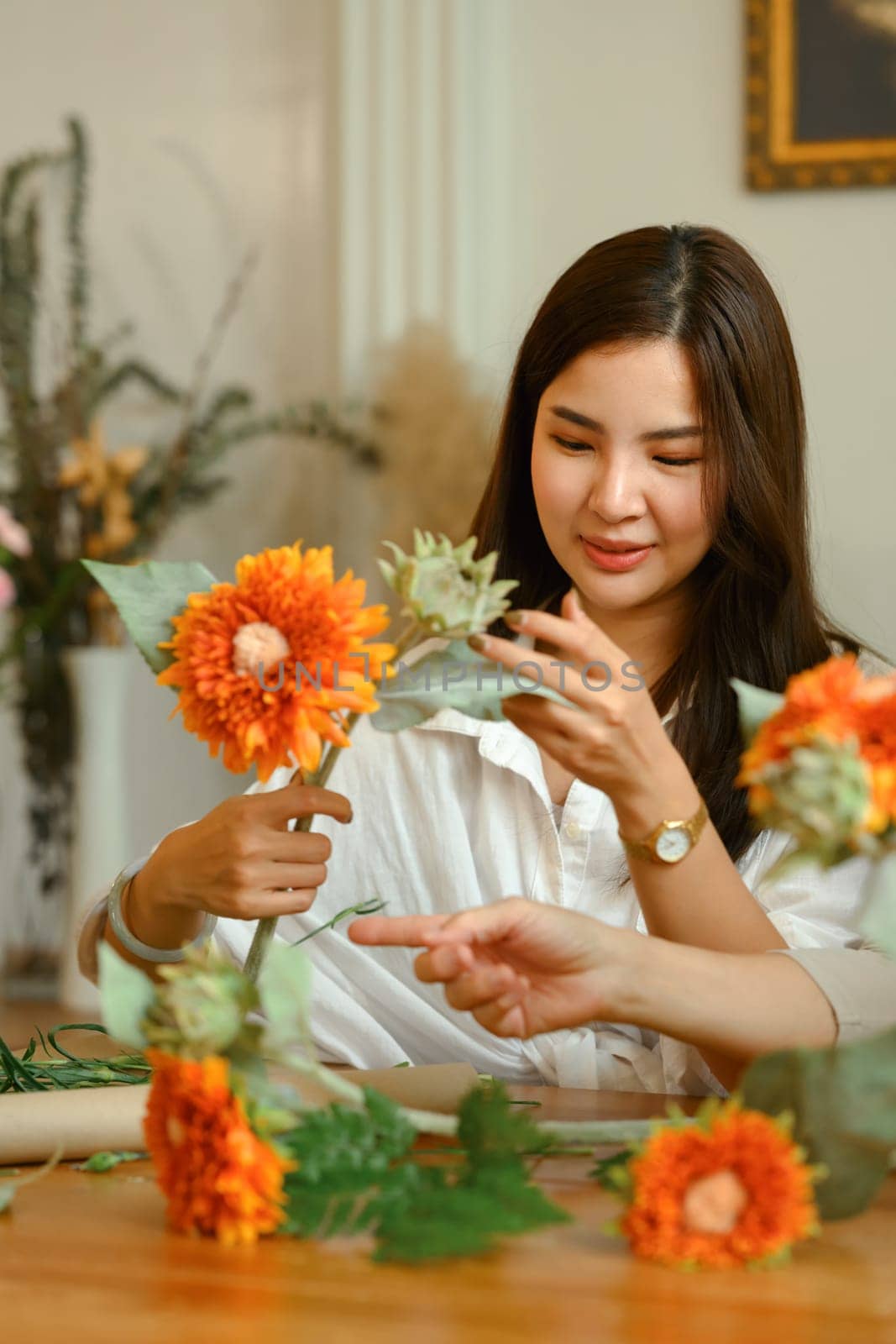Pleasant Asian woman making a bouquet with fresh flowers at floral shop. Floristry and small business concept.