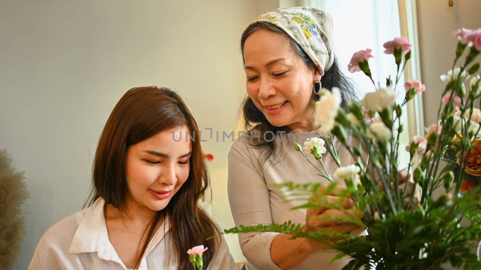 Smiling middle age female florist preparing bouquet of pink flowers at table in flower shop. Floristry and small business concept.