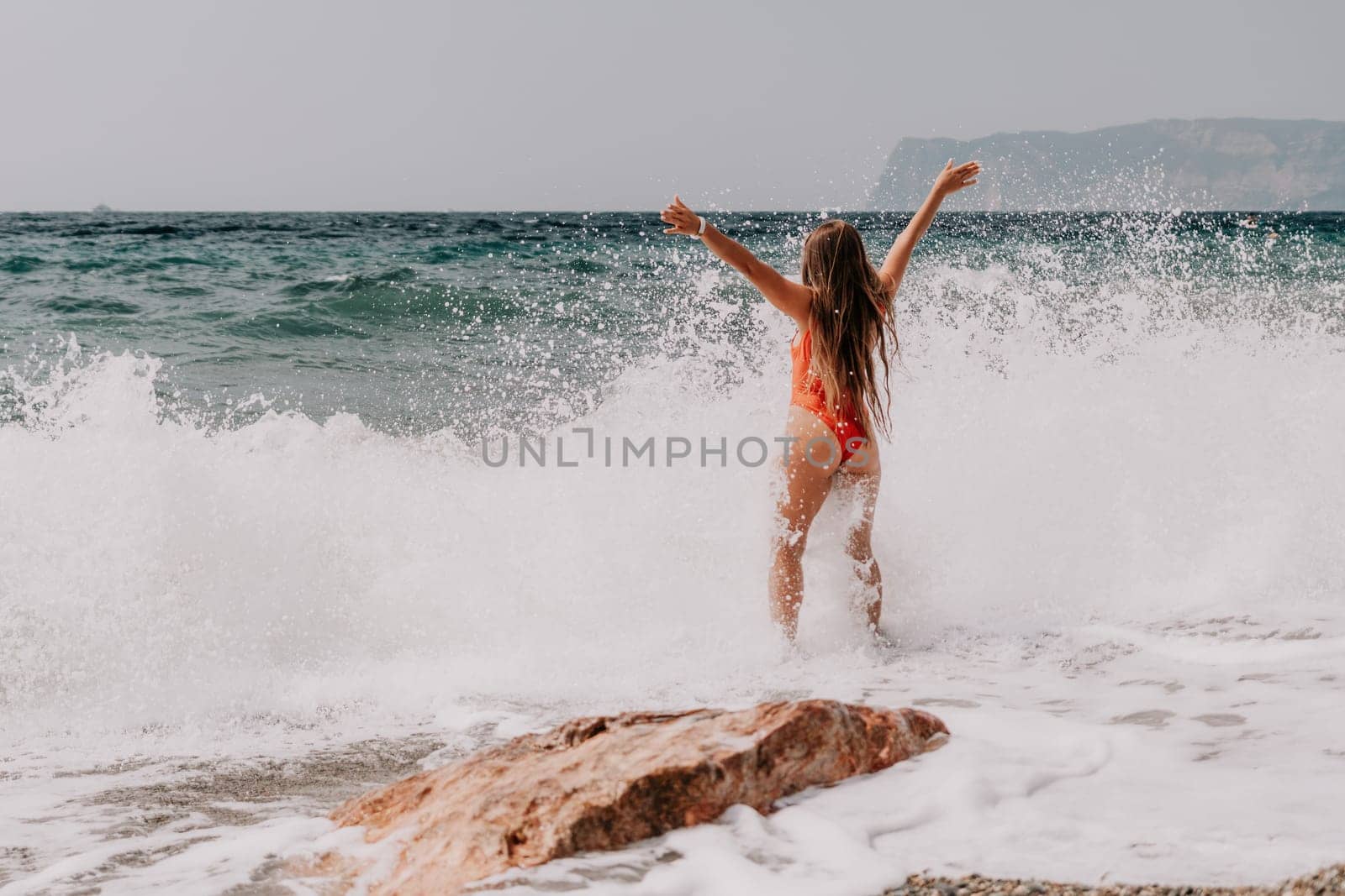 Woman travel sea. Young Happy woman in a long red dress posing on a beach near the sea on background of volcanic rocks, like in Iceland, sharing travel adventure journey