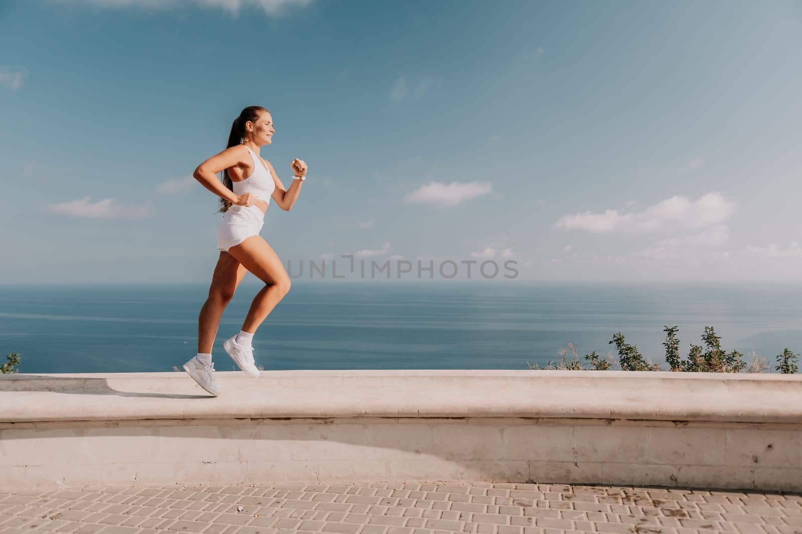 Fitness woman sea. Active, happy middle-aged woman in white sportswear exercises outdoors in a park over sea. Healthy lifestyle, physical activity and female fitness pilates and yoga routines. by panophotograph