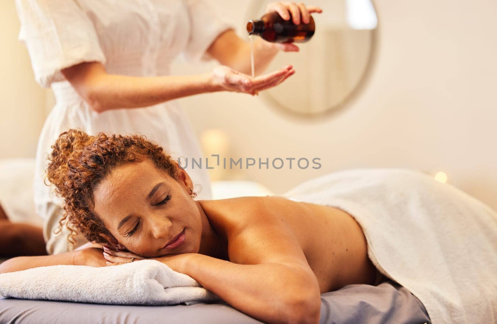 Spa, luxury massage and woman with essential oil getting back massage for wellness in beauty salon. Health, beauty and black woman with massage therapist for relaxation, stress relief and body care by YuriArcurs