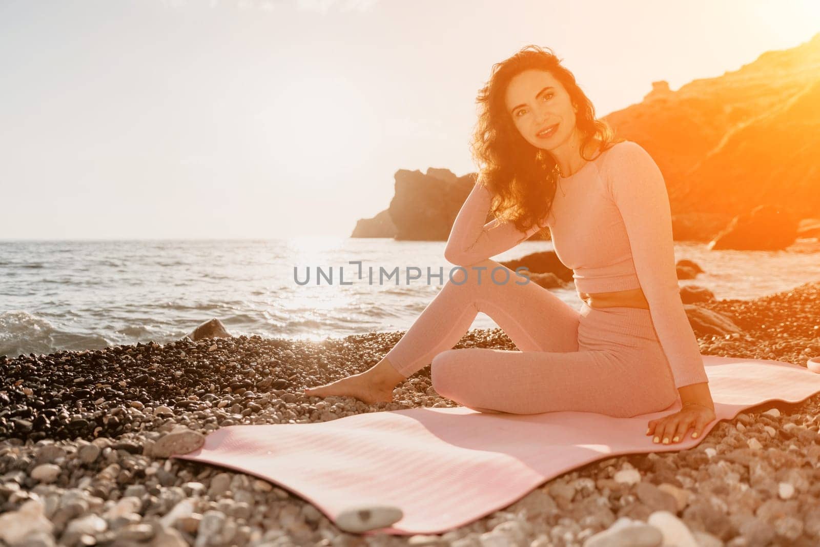 Woman sea yoga. Happy woman with black hair doing Pilates with the ring on the yoga mat near the sea on the pebble beach. Female fitness yoga concept. Healthy lifestyle, harmony and meditation. by panophotograph